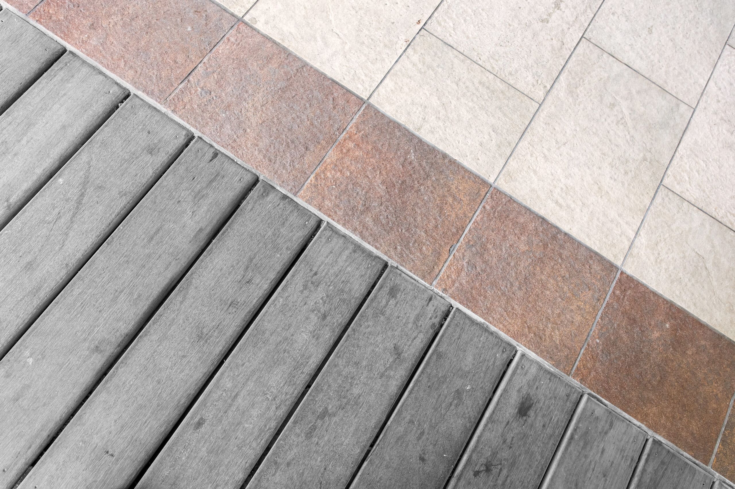 Sol extérieur divisé en diagonale, combinant lames de bois gris usé, une bande de carrelage terre cuite et du carrelage crème.