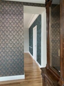 Couloir élégant avec papier peint à motifs de cercles verts/beiges et un autre géométrique vert. Sol parquet clair, meuble bois foncé.
