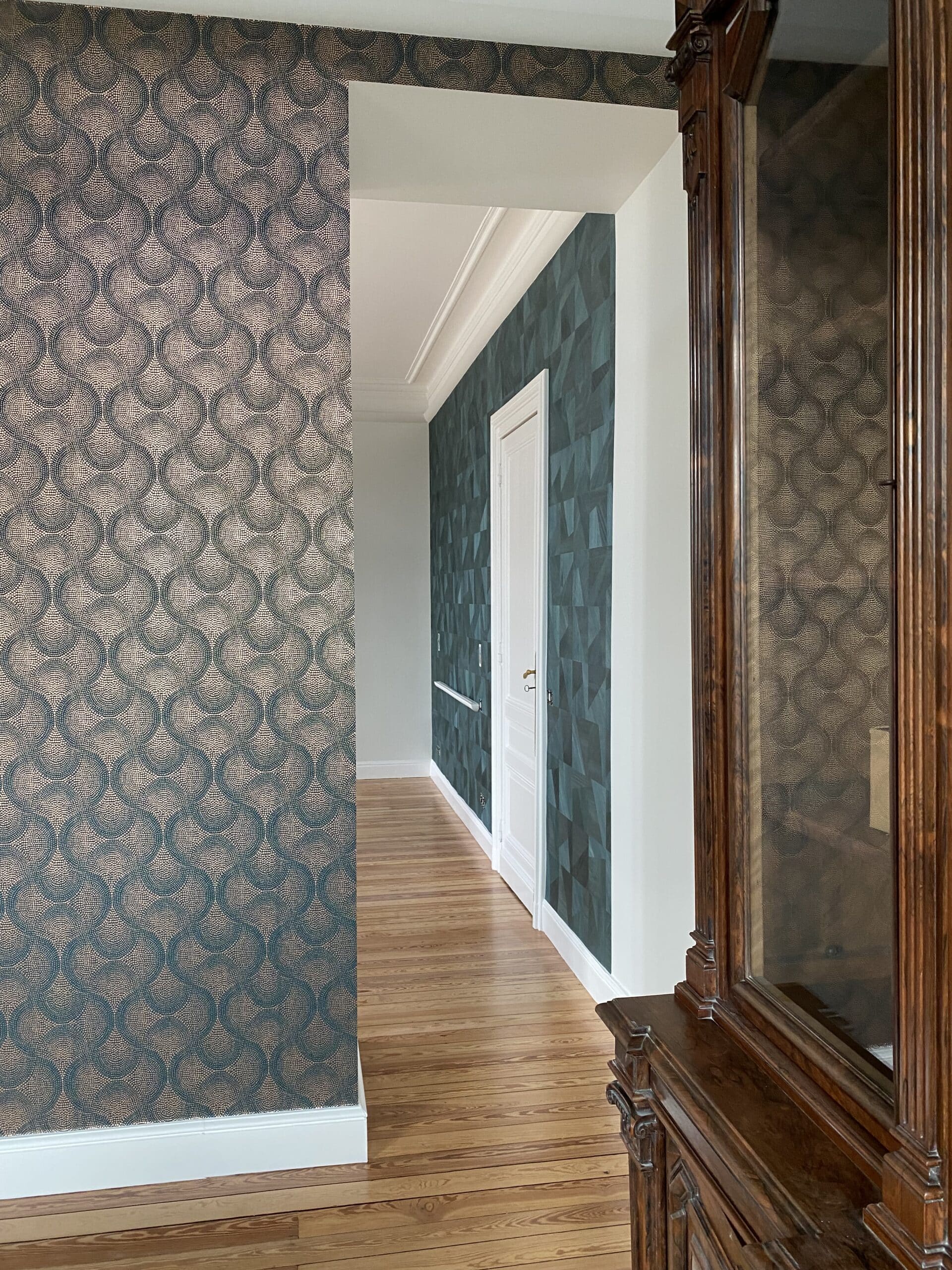 Couloir élégant avec papier peint à motifs de cercles verts/beiges et un autre géométrique vert. Sol parquet clair, meuble bois foncé.