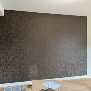 Mur marron avec papier peint texturé à motifs géométriques 3D dans un intérieur moderne. Sol bois clair, plinthes blanches et carrelage décoratif.