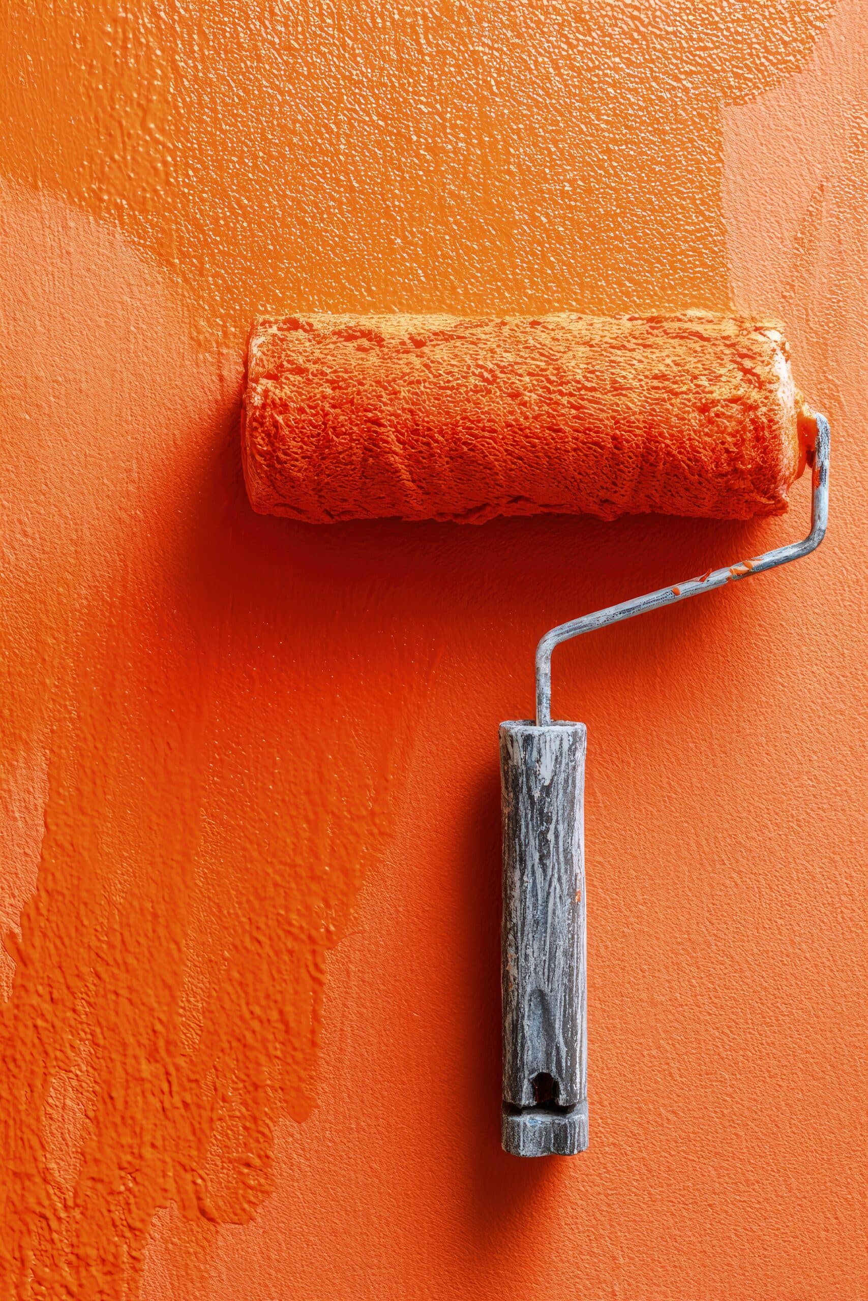 Rouleau de peinture orange vif sur un mur texturé. La peinture fraîche laisse une surface riche et vibrante.