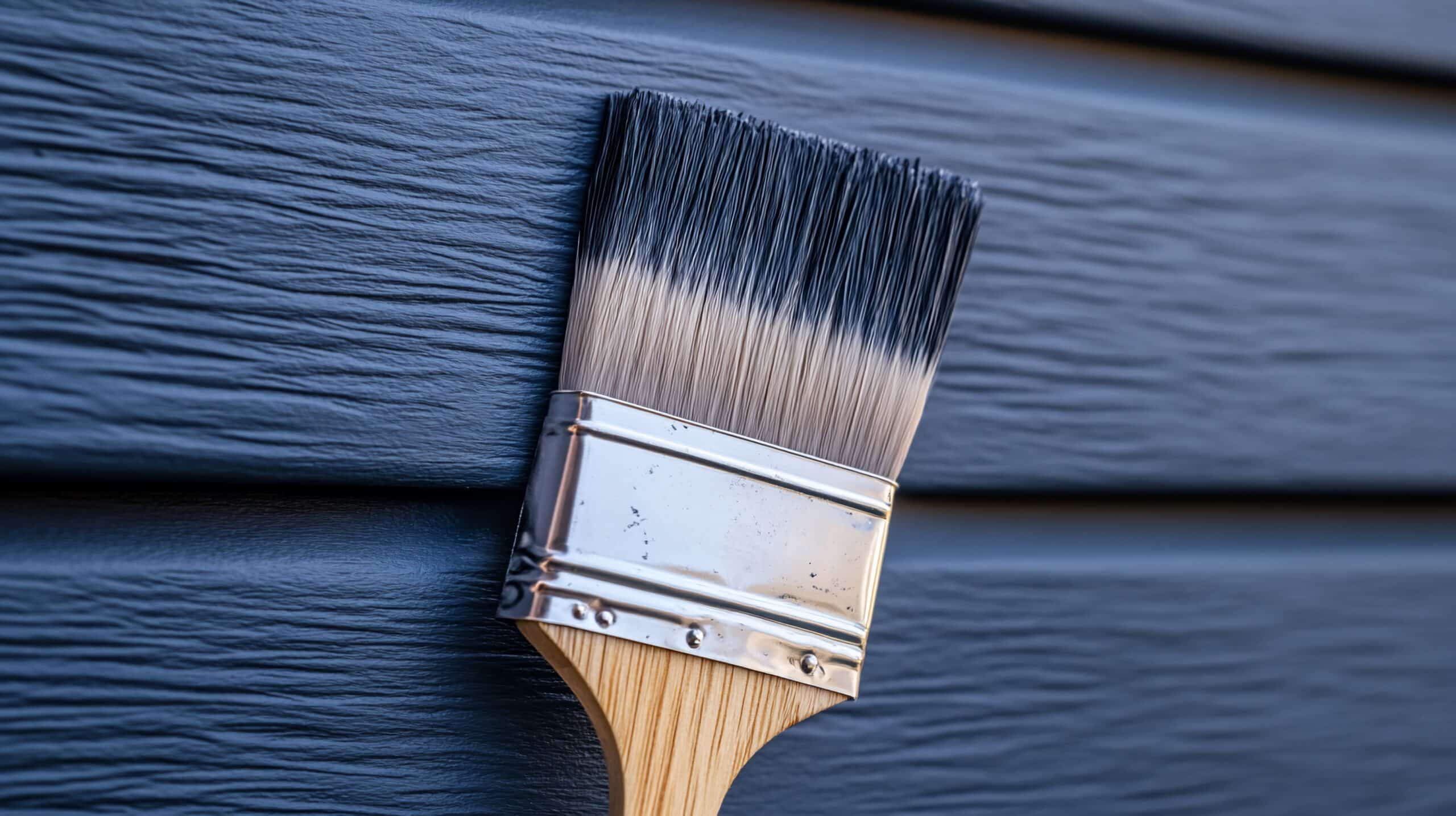Pinceau propre à manche en bois et virole argentée, ses soies bicolores touchant un revêtement mural bleu foncé texturé, prêt à peindre.